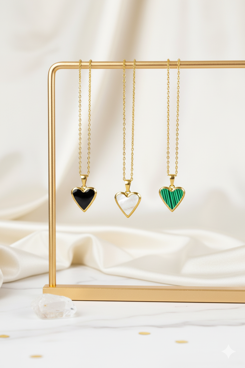 Three heart-shaped pendants on gold necklaces displayed on a gold stand against a white background.