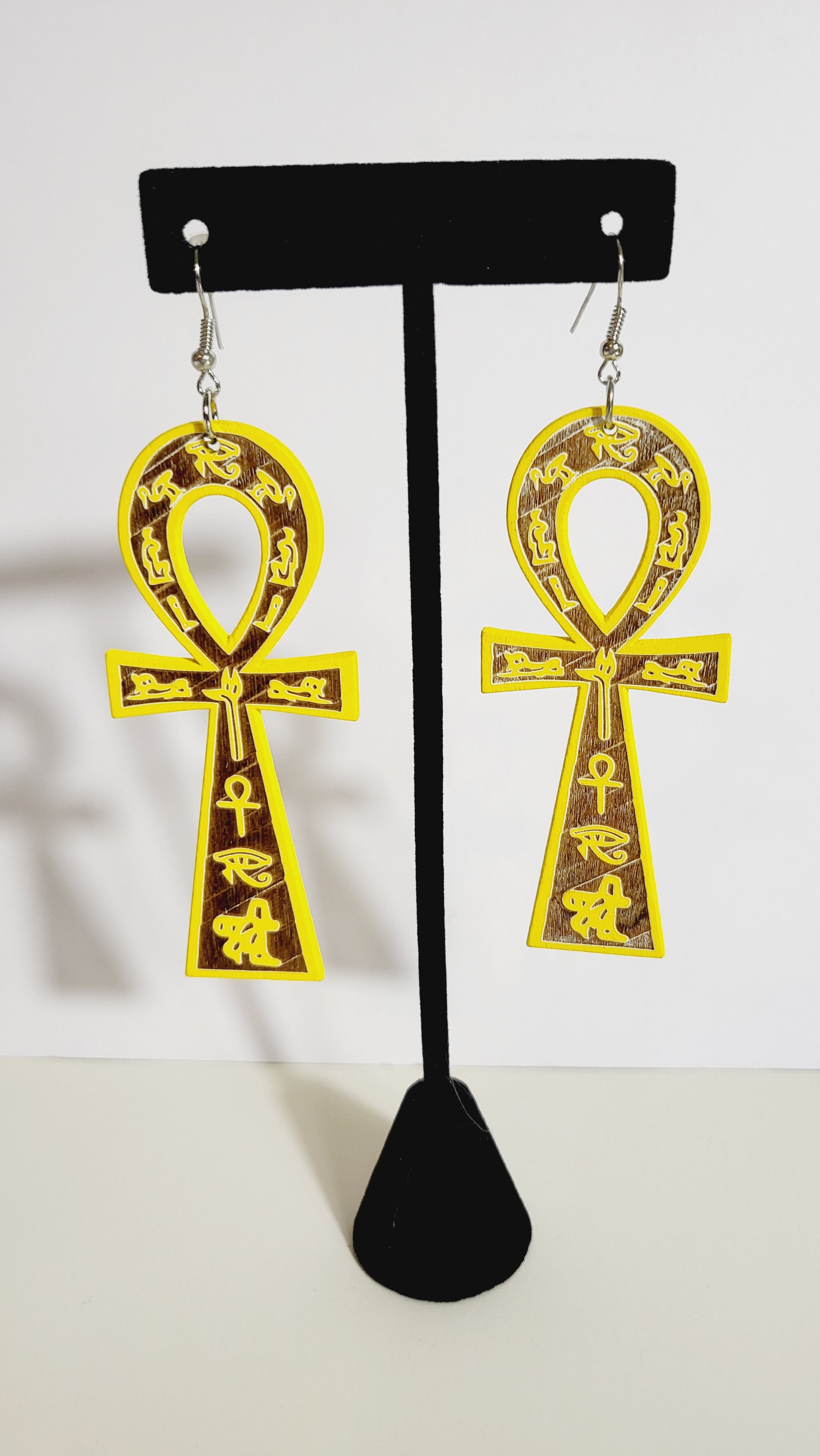 A pair of yellow ankh earrings with brown and gold accents displayed on a mannequin.