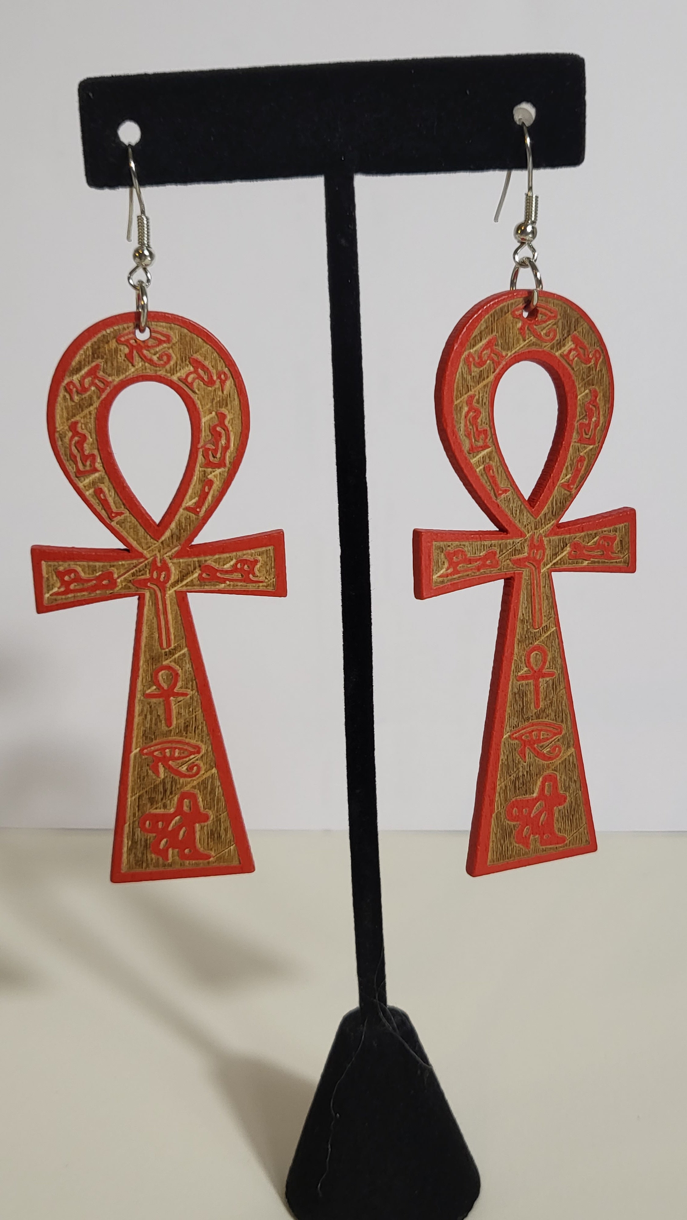 A pair of ankh earrings with brown and gold accents displayed on a mannequin.