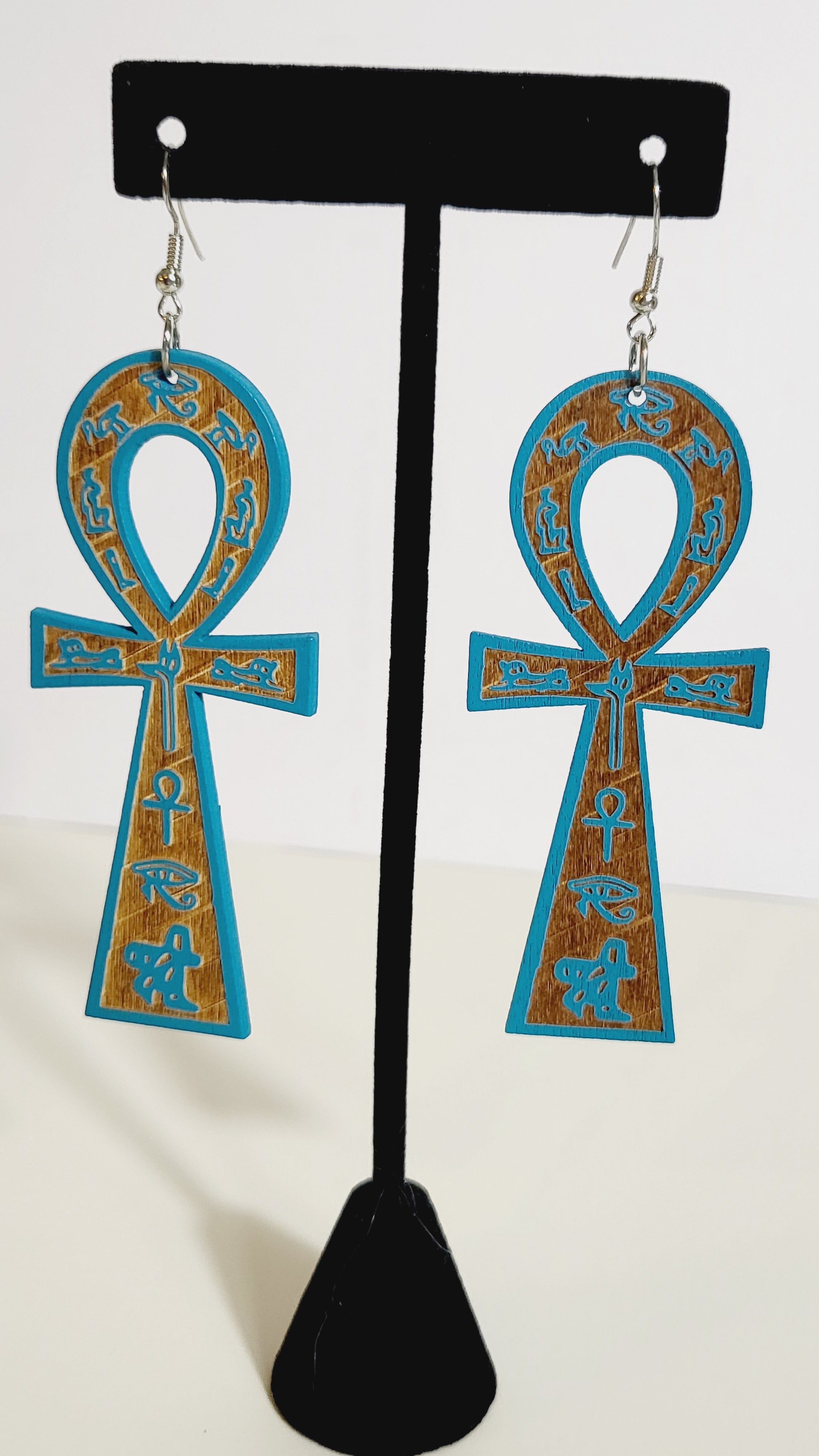 A pair of ankh earrings with brown and gold accents displayed on a mannequin.