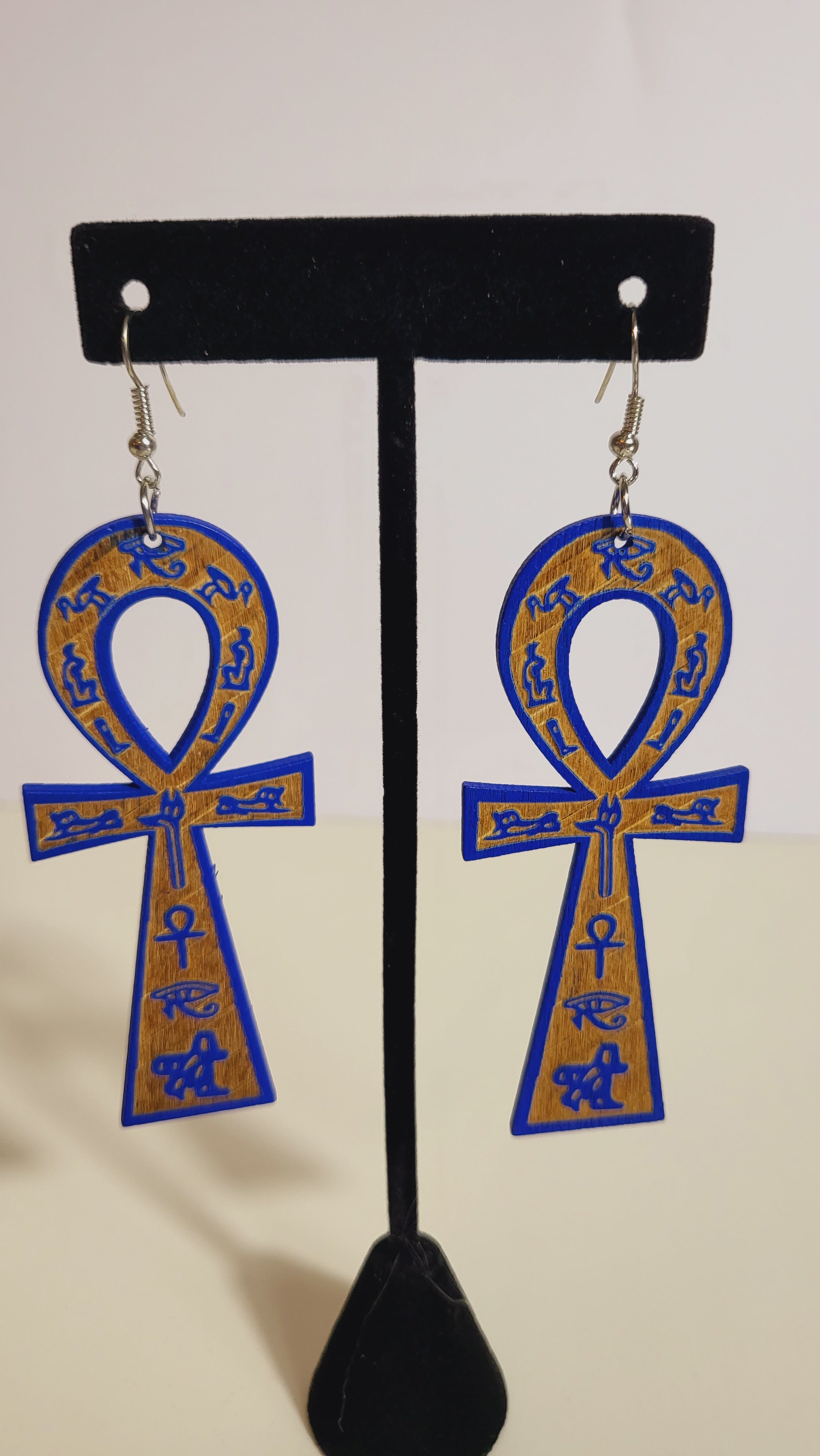 A pair of ankh earrings with brown and gold accents displayed on a mannequin.