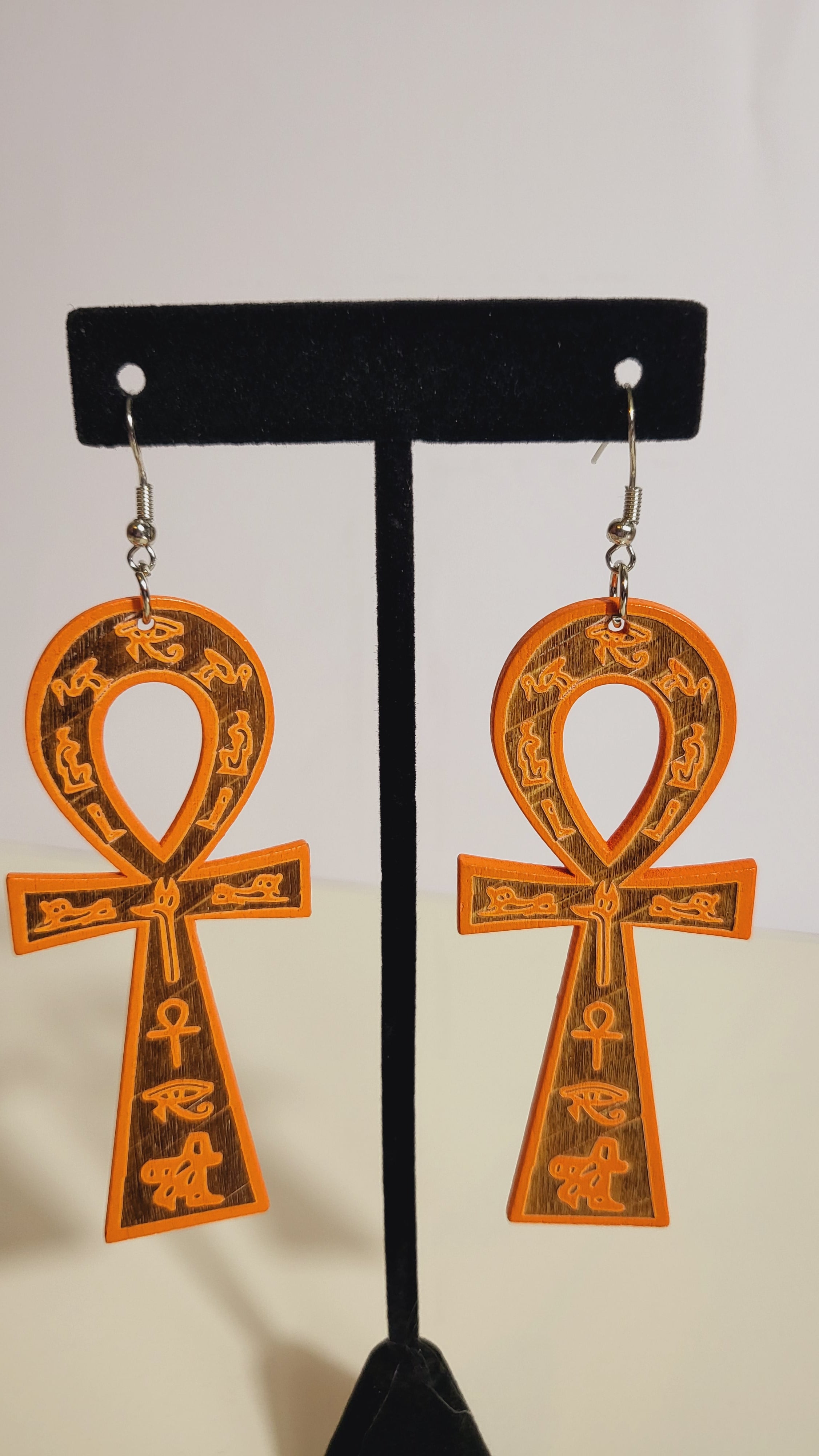 A pair of ankh earrings with brown and gold accents displayed on a mannequin.