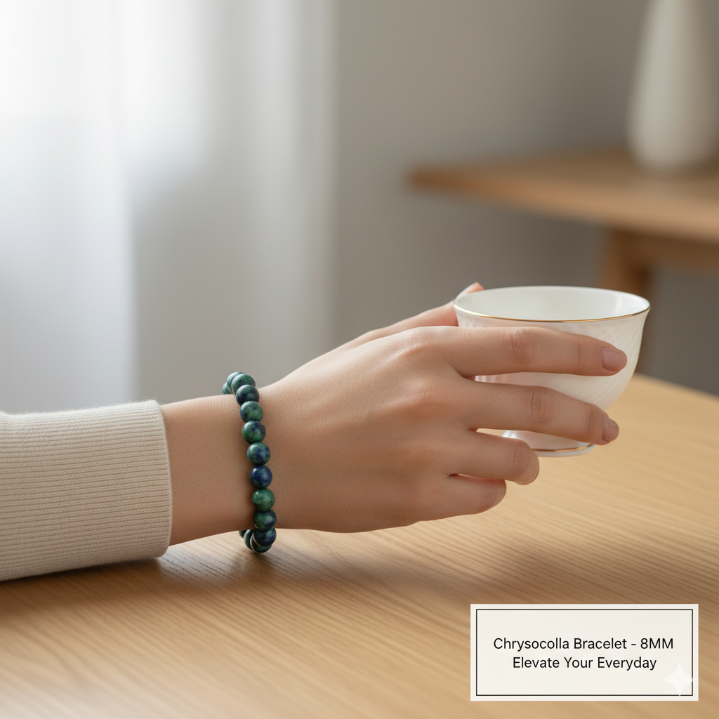 Hand holding a small white cup with a green chrysocolla bracelet on a wooden surface.